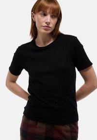 T-shirt noir côtelé à manches courtes avec un col rond, une coupe ajustée et un tissu texturé, associé à une jupe à carreaux.