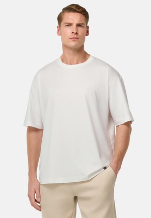 Weißes Baumwoll-T-Shirt mit Rundhalsausschnitt, kurzen Ärmeln und lockerer Passform. Verfügt über ein kleines Markenetikett an der Seite.