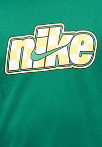 Tissu vert avec un logo "nike" à carreaux jaunes et blancs, comprenant un swoosh vert traversant les lettres.