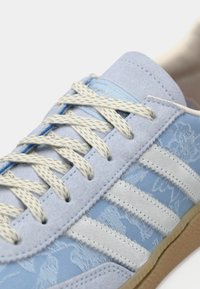 Baskets en daim bleu avec des accents bleu clair et un design texturé. Elles présentent des lacets de couleur crème et trois bandes blanches sur le côté.