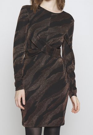 Kobieta w długiej sukience z czarno-brązowym metalicznym wzorem tygrysich pasków, z drapowaniem w talii.