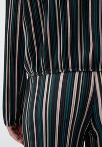 Set di tessuti a strisce multicolori in tonalità teal, nero e beige. La texture appare liscia con un dettaglio di vita elasticizzata arricciata.