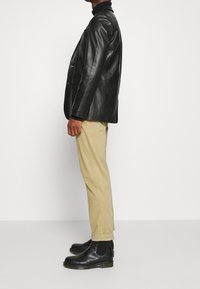 Svart skinnblazer, beige avsmalnande byxor och svarta Chelsea-boots. Mjuk textur, figursydd design, minimal detaljering med metall.