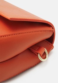 Oranžová kožená kabelka s hladkým povrchem, s překlopnou klopou a zlatým kovovým kroužkem.