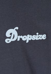 Mørkegrå stof med en glat tekstur, der har den hvide, stiliserede tekst "Dropsize" tydeligt fremhævet i midten.