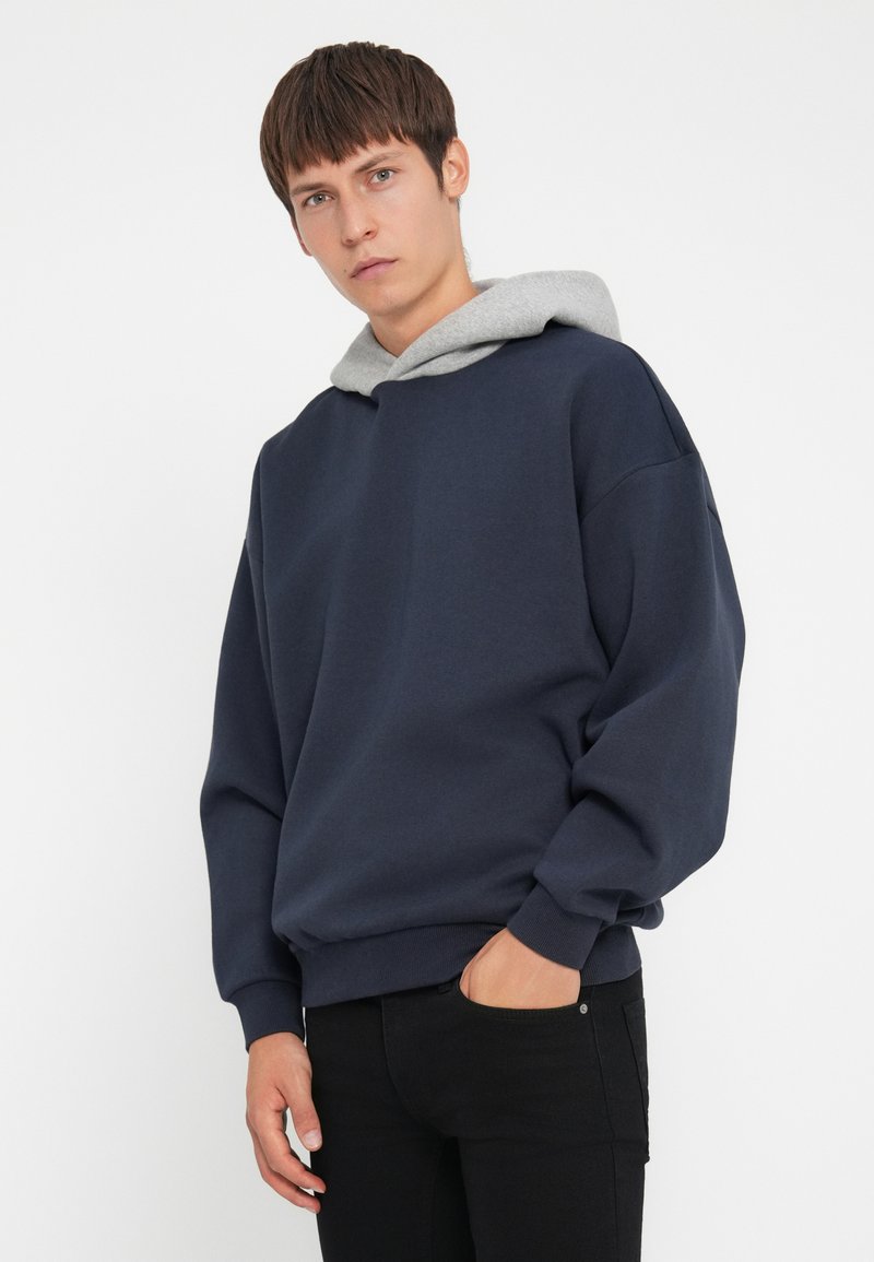 Marineblaues Sweatshirt mit grauem Kapuzen, oversized Schnitt, gerippte Bündchen und Saum. Weicher, strukturierter Stoff mit einem lässigen Design.