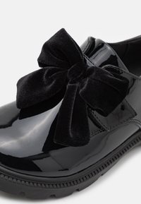 Schwarze Lacklederschuhe mit runder Spitze, ausgestattet mit einer großen schwarzen Samtschleife auf der Vorderseite und einer strukturierten Gummisohle.