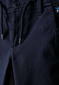 Pantaloni blu navy realizzati in tessuto misto cotone, con vita regolabile tramite cordoncino, chiusura con bottone e una trama sottile, completati da un'etichetta laterale.