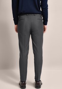 Gray tailored trousers in fabric with a smooth texture, tapering fit, and rear pockets; worn with a navy sweater and dark shoes.