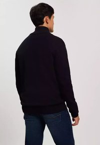 Czarny sweter z golfem, prążkowany dekolt i brzeg, miękka dzianina, dopasowany krój, noszony z niebieskimi dżinsami, widok z tyłu.