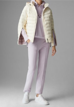 Kräppjacka i krämfärg med kviltad design, tillsammans med en lila huvtröja och matchande joggers, avslutad med vita sneakers.