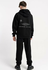 Czarny zestaw z hoodie i dresów, z tekstem na plecach, ściągaczami przy rękawach i kieszenią kangurką. Wykonany z miękkiego materiału.