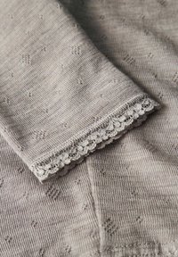 Grått stickat tyg med ett strukturerat mönster, prytt med en fin spetskant i fållen. Mjukt, lätt material med subtila detaljer.
