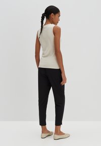 Débardeur en crème à côtes, pantalon noir fuselé et mocassins beiges. Design minimal sans motifs. Texture lisse, silhouette ajustée.