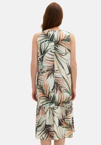 Robe sans manches avec un imprimé de feuilles tropicales dans des tons de vert, marron et pêche. Le design comprend une jupe à volants et une texture de tissu légère.