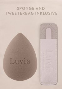 Druppelvormige make-upspons met het label "Luvia" naast een witte leren pincettetas met gestikte randen en een trekkoord.