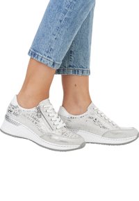 Baskets blanches avec des accents métalliques, présentant un dessus texturé avec des mots imprimés, un laçage à l'avant et une semelle blanche épaisse.