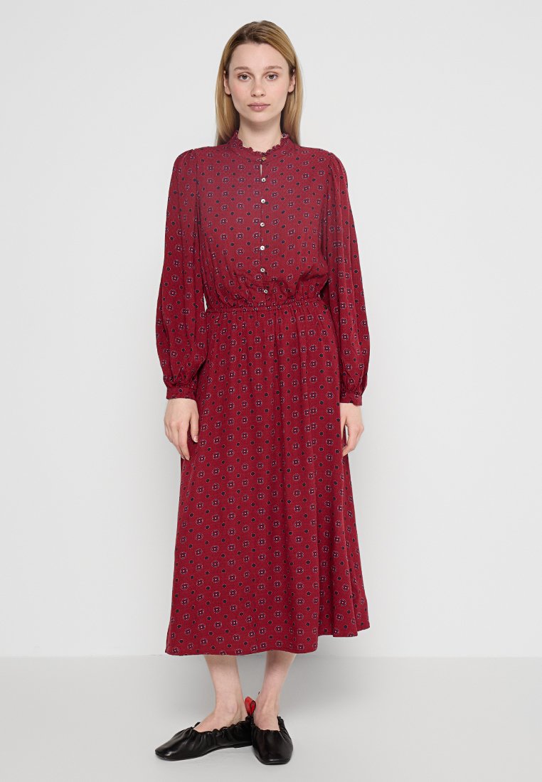 Rotes Midi-Kleid mit floralem Muster, langen Ärmeln, Knopfleiste und elastischem Bund. Weicher Stoff mit leichtem Glanz. Schwarze flache Schuhe.
