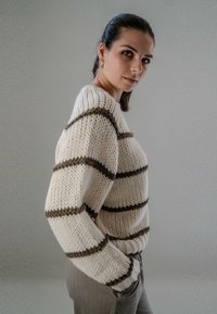Chunky gebreide trui in roomkleur met donkerbruine horizontale strepen. Heeft een relaxte pasvorm, ronde halslijn en een gestructureerde stof.