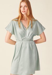 Vestido de manga corta en tejido verde claro con patrones hexagonales, con escote en V, cintura ceñida y falda acampanada. Textura suave.