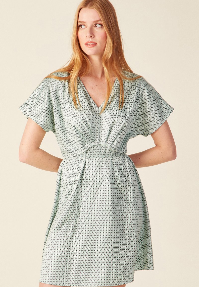 Vestido de manga corta en tejido verde claro con patrones hexagonales, con escote en V, cintura ceñida y falda acampanada. Textura suave.