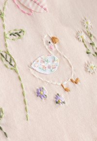 Diseño bordado en tela rosa suave que presenta un pato en tela con patrón floral, rodeado de hojas verdes y flores moradas.