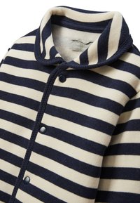 Cardigan rayé bleu marine et crème, présentant un tissu doux et texturé, un col arrondi, une fermeture à boutons et des détails de couture visibles.