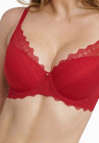 Red lace bra featuring a scalloped edge and smooth fabric cups, with a decorative gold accent at the center. Textured and fitted design.