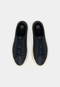 Zapatillas de cuero azul marino con punta redonda, cordones planos y suela de goma beige. Presentan un logotipo en las plantillas y una parte superior texturizada.