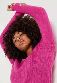 Suéter fucsia con un corte holgado, mangas anchas y un tejido texturizado y esponjoso. Presenta un escote en V y está fabricado con un material suave y acogedor.