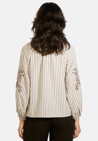Blusa rigata in beige e crema, con ricami floreali sulle maniche e polsini elasticizzati. Tessuto morbido con una vestibilità comoda.