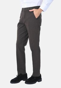 Pantaloni a gamba dritta grigio scuro con una texture liscia, dotati di tasche frontali e chiusura con bottone, abbinati a scarpe in suede nere.