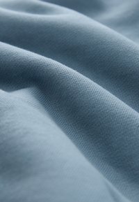 Pehme sinakashall kangas, mille peen kudumustruktuur näitab õrnu voldikuid ja varje, luues sileda ja hubase ilme.