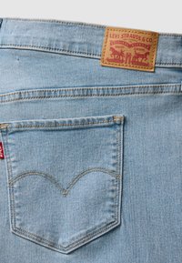 Jean en denim bleu clair avec poche arrière, étiquette rouge Levi's et étiquette en cuir marron présentant deux chevaux et détails de marque.