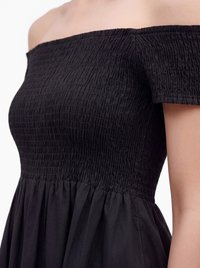 Sort off-shoulder kjole med smocket krop og korte ærmer, tætsiddende øverst og flydende nederdel under taljen.
