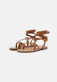 Sandalias planas marrones con tiras de cuero entrelazadas y hebilla en el tobillo. Plantilla suave y diseño minimalista. Sin tacones, estilo casual.