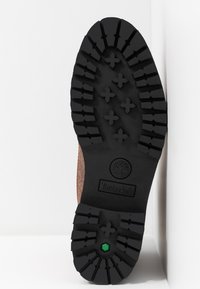 Semelle de botte Timberland en caoutchouc noir avec des crampons profonds, des motifs en forme de croix et un détail hexagonal vert près du talon.