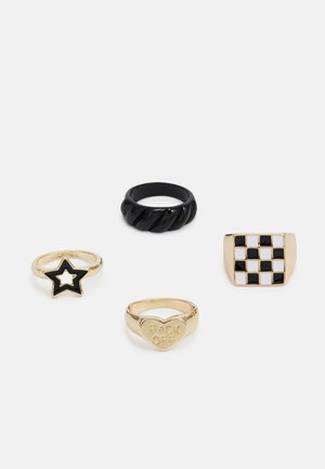 Quatro anéis: uma banda torcida preta, uma estrela dourada com esmalte preto, um coração dourado inscrito "F**K OFF" e um anel dourado com padrão de xadrez.