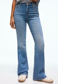 Jean évasé bleu clair en denim avec une taille haute, présentant un style classique à cinq poches et une texture légèrement délavée.