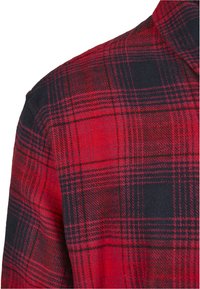 Rød og svart rutete flanellskjorte, med en teksturert stoff og et sjakkmønster, og en krage som er delvis synlig.