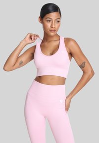 Różowy sportowy stanik i legginsy z wysokim stanem uszyte z elastycznej, gładkiej tkaniny. Oba elementy mają logo oraz prosty, bezszwowy design.
