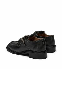Scarpe in pelle nera con punta arrotondata, chiusura con fibbia e perforazioni decorative. Finitura testurizzata e dettagli di cucitura discreti.
