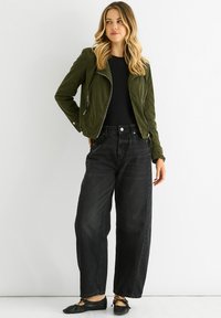 Olive green corduroy biker jacket with asymmetrical zipper, black fitted top, high-waisted black denim trousers, and black flats.