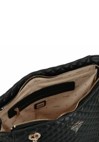 Borsa a tracolla nera trapuntata con zip e accessori dorati. L'interno presenta una fodera beige chiaro con un motivo ripetuto "GUESS" e tasche.