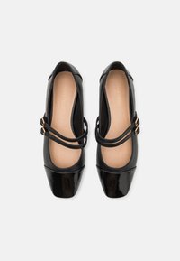 Schwarze Lackleder-Ballettflats mit spitz zulaufender Zehenpartie, zwei schmalen Riemen und goldfarbener Hardware. Glatte Innenausstattung und minimale Designelemente.