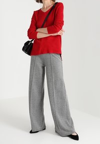 Pull à manches longues rouge côtelé associé à un pantalon large à motif pied-de-poule gris. Sac à main noir structuré et ballerines noires pointues.