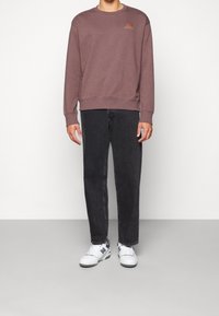 Vinröd sweatshirt med ribbstickade muddar och krage, med en liten orange logotyp, kombinerad med svarta jeans och vita sneakers.