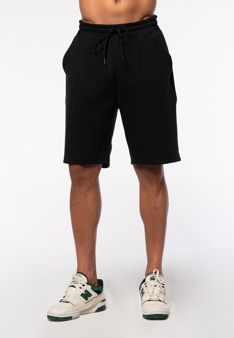 Black cotton shorts with an elastic waistband and drawstring. The design features a relaxed fit, reaching just above the knee.