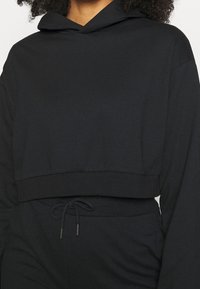 Bawełniana krótka bluza z kapturem w jednolitym czarnym kolorze z detalem sznurka na dole i miękką teksturą; ma długie rękawy i kieszeń z przodu.