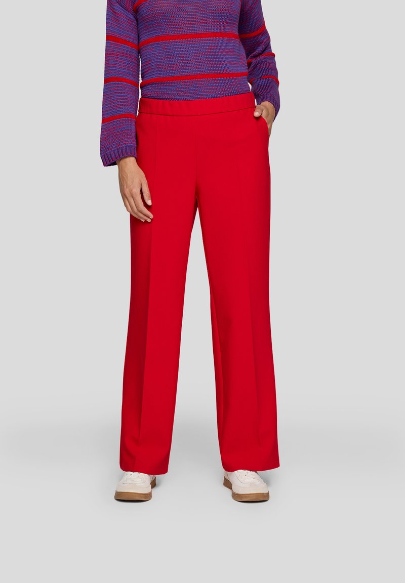 Red wide-leg pants made of smooth fabric with a high waist. Model wears a blue and purple striped sweater. White sneakers on feet.